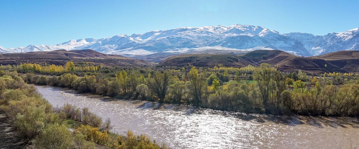 A river flowing through a valley with snow-capped mountains in the background.