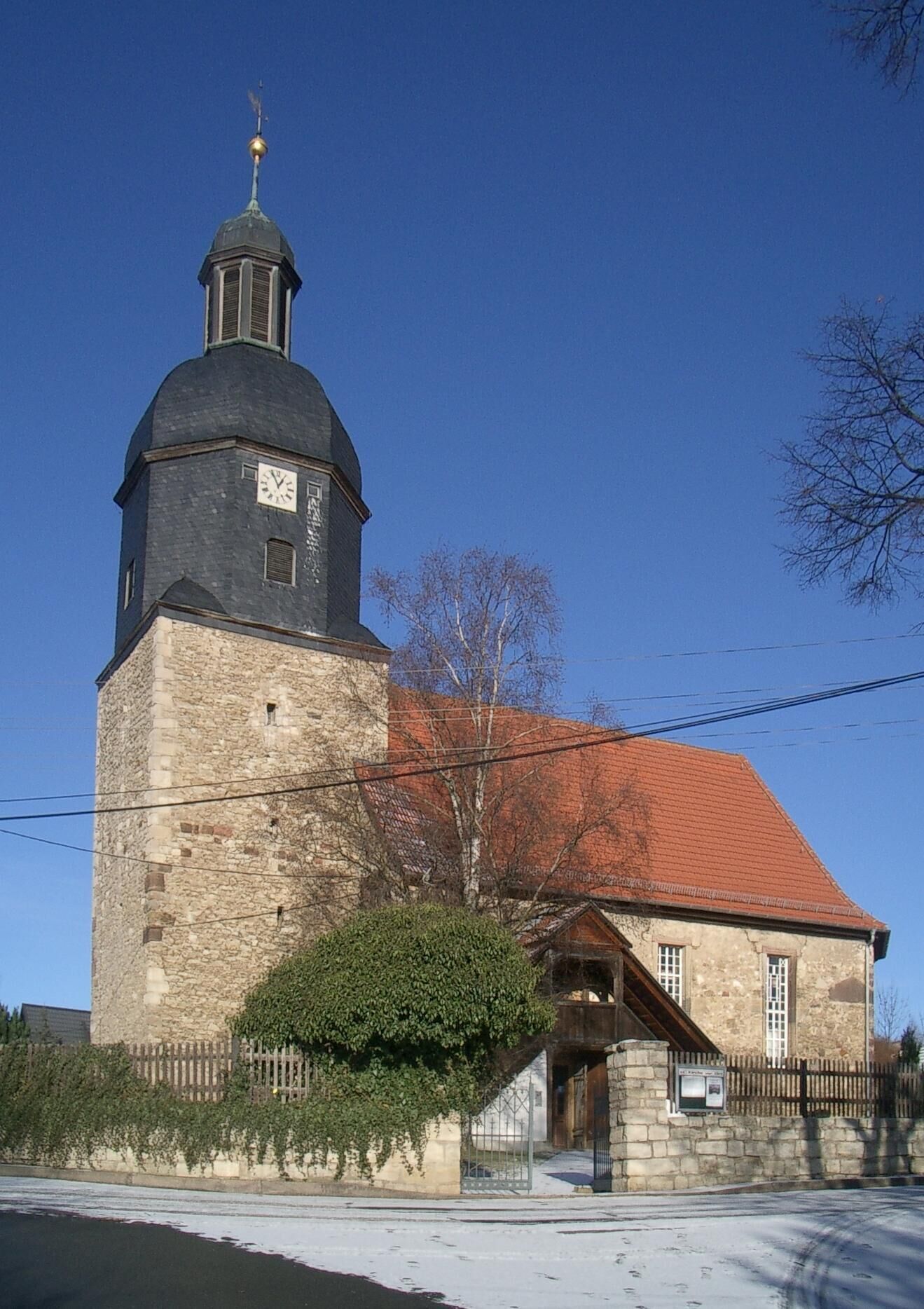 A church with a stone tower and a red-roofed building.