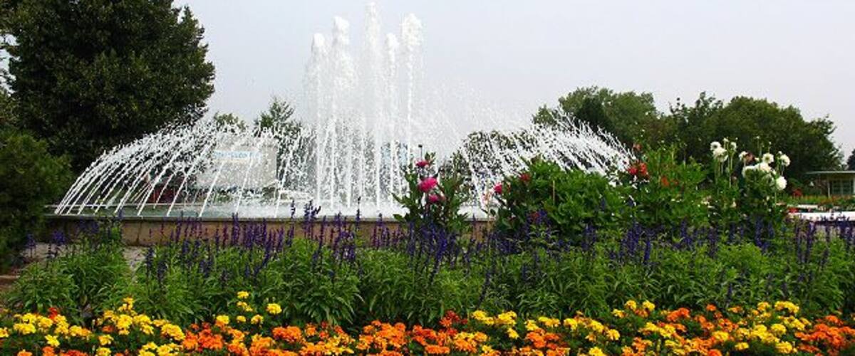 A fountain with water jets, surrounded by colorful flower beds.