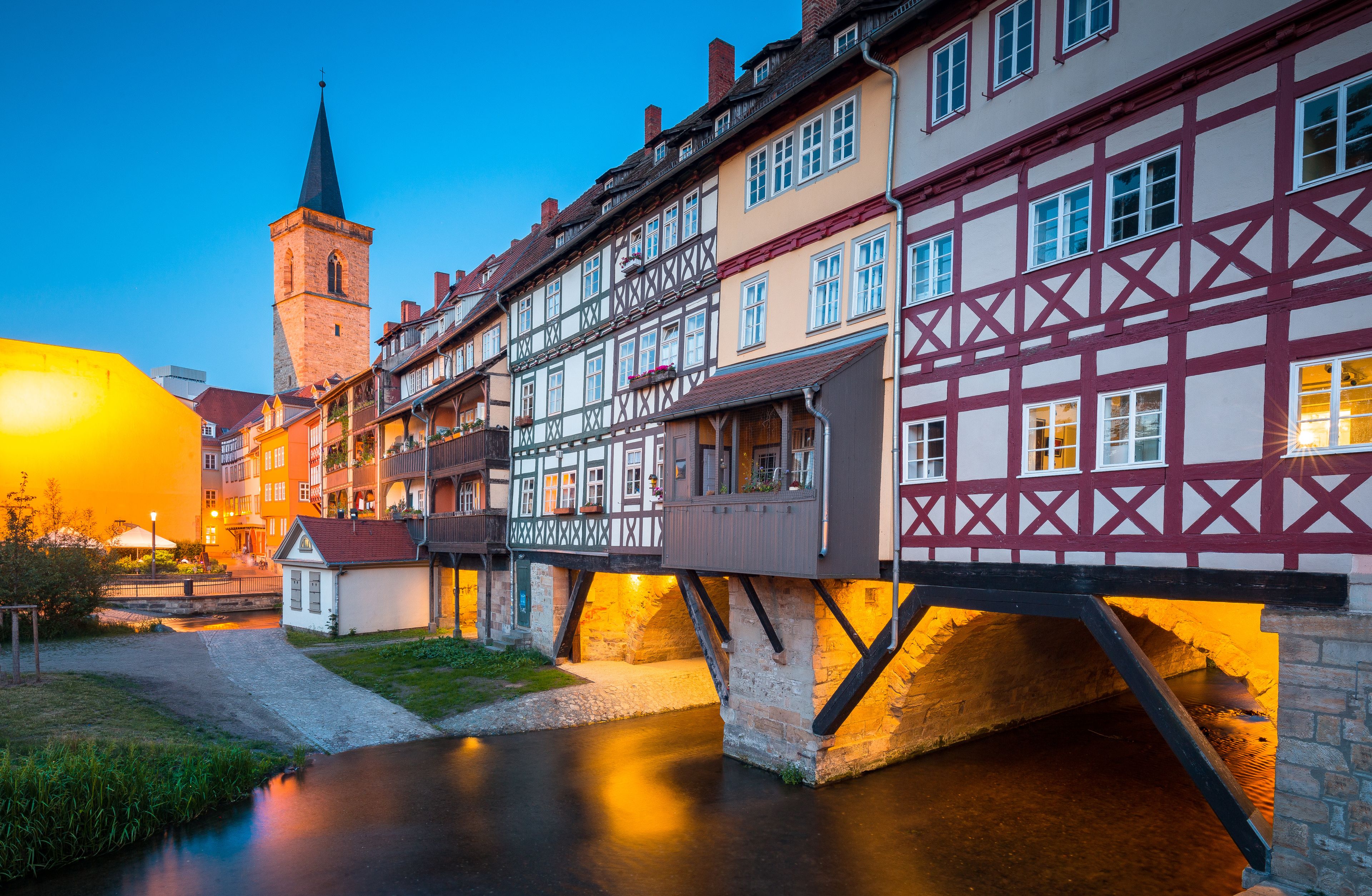 A riverside town with traditional half-timbered houses, a church tower, and a pedestrian bridge.