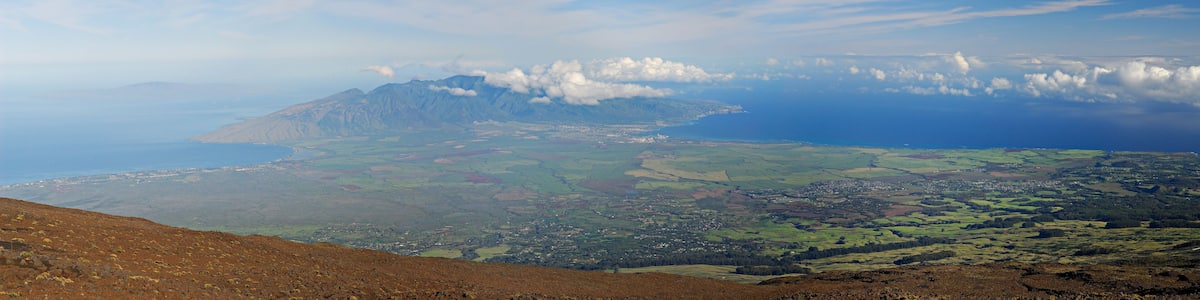 Un paysage montagneux avec une ville nichée au creux de collines ondoyantes et une côte visible au loin.