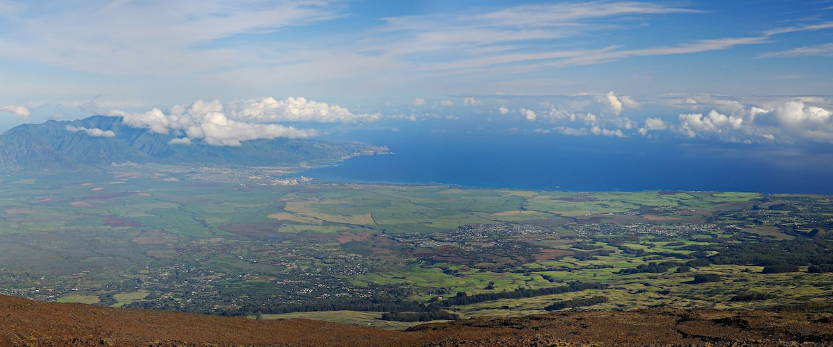 Un paisaje montañoso con un pueblo ubicado entre colinas ondulantes y una costa en la distancia.