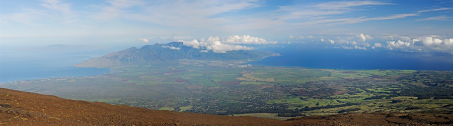 A mountainous landscape with a town nestled among rolling hills and a coastline in the distance.