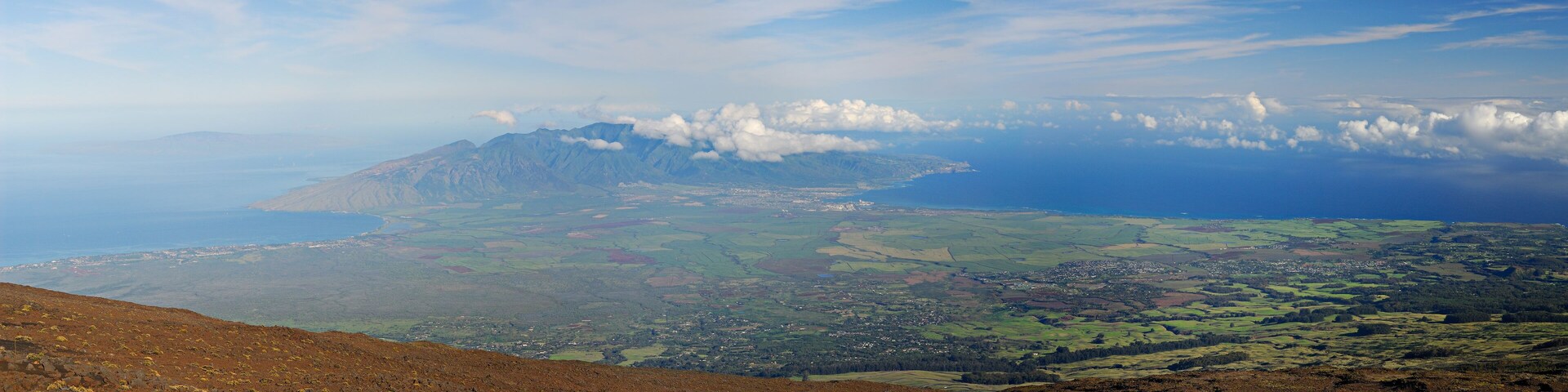 A mountainous landscape with a town nestled among rolling hills and a coastline in the distance.