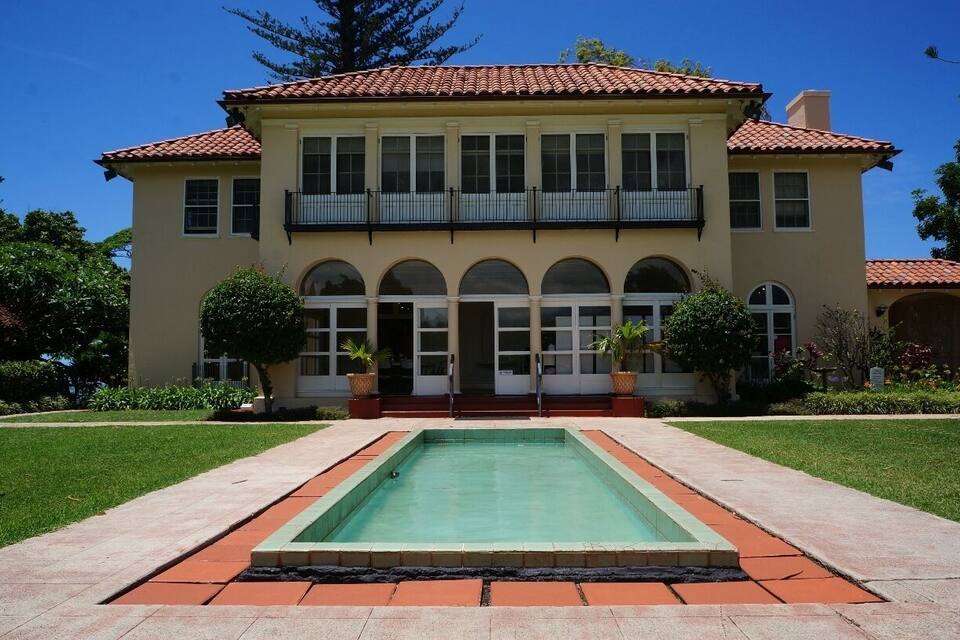 A large two-story house with a swimming pool in front.