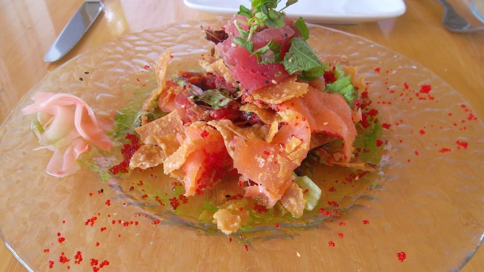 A dish with salmon, greens, and a pink garnish on a glass plate.