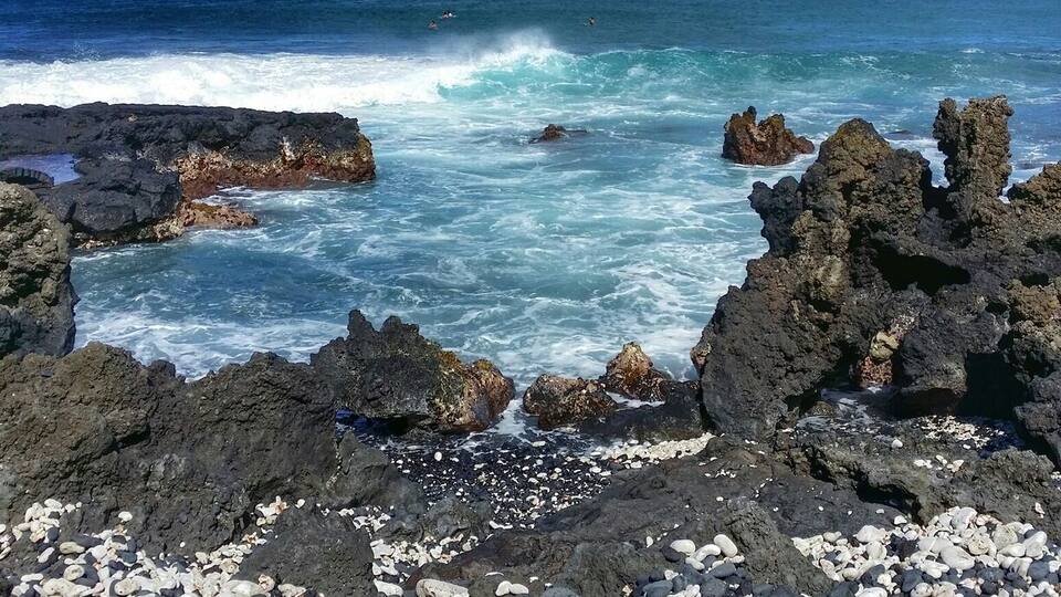 A rocky shoreline with waves crashing against the rocks and pebbles.