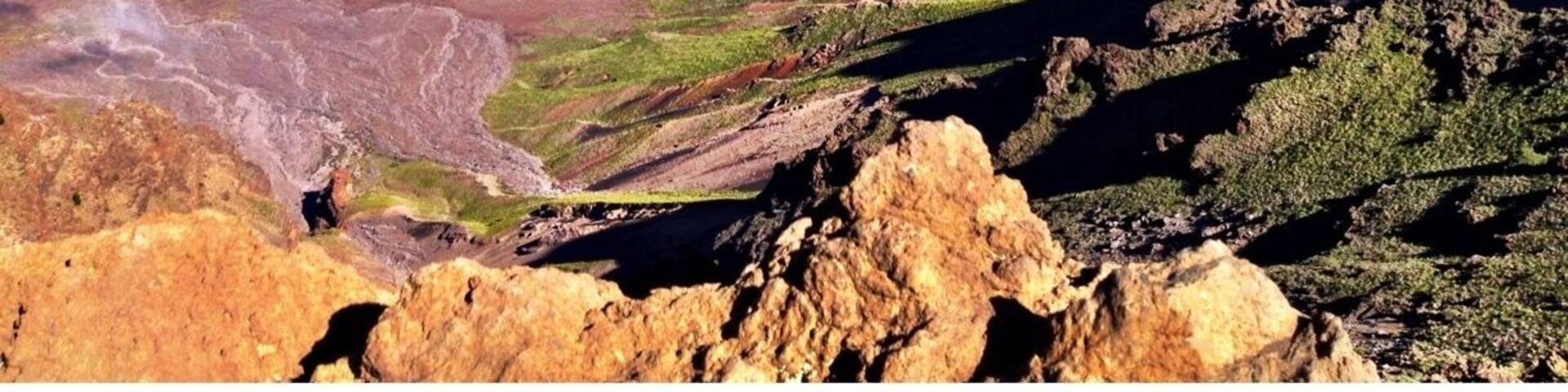 A volcanic landscape with rugged terrain, green valleys, and reddish-brown hills.