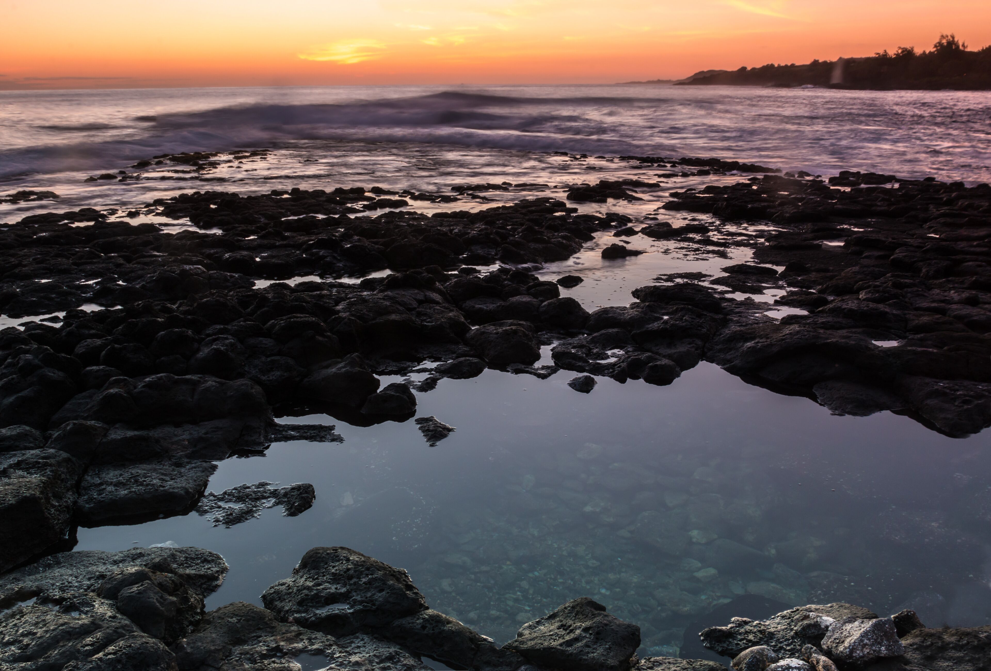 Una costa rocosa con aguas cristalinas que reflejan el atardecer.