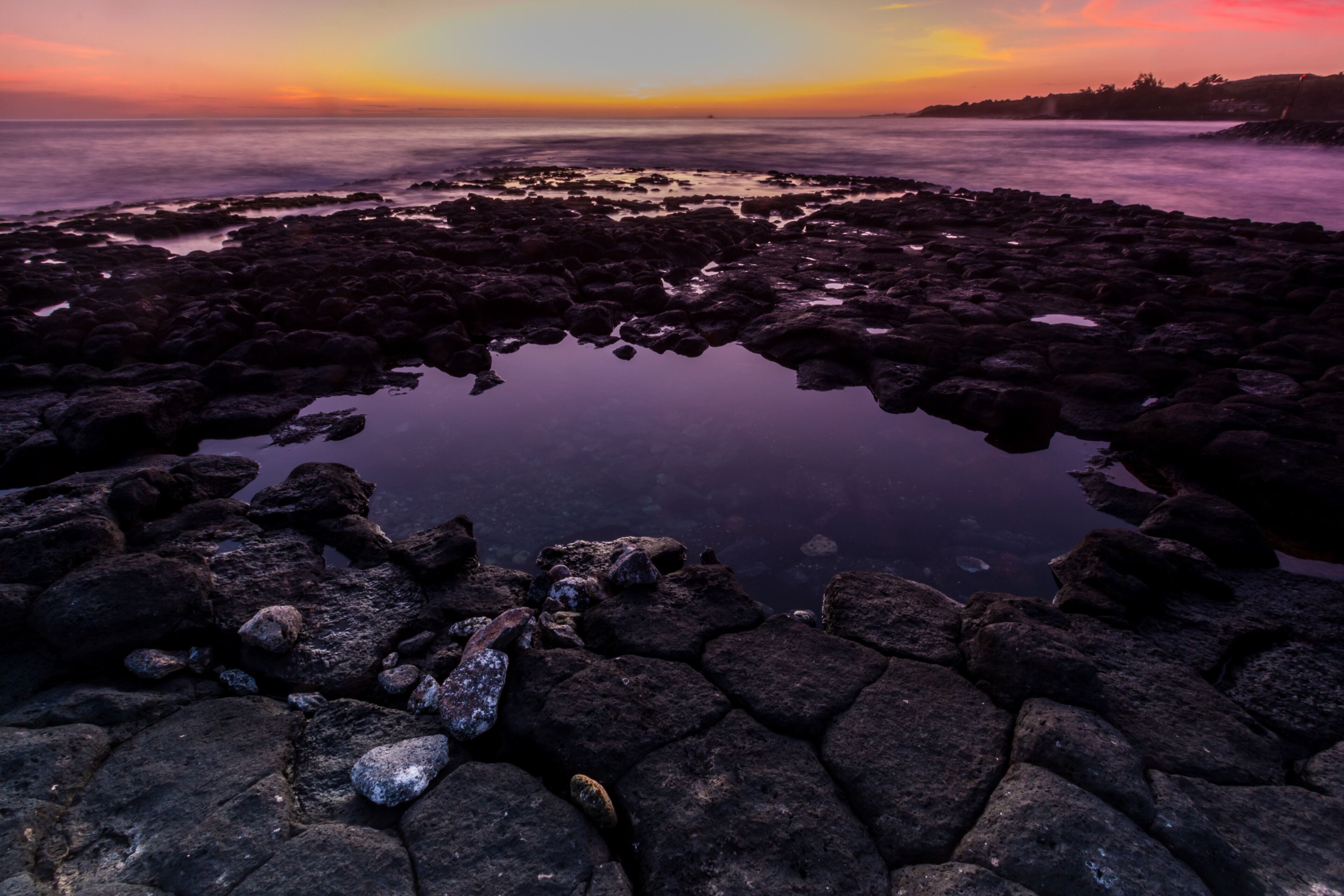 A rocky shoreline with a calm body of water reflecting the sunset.