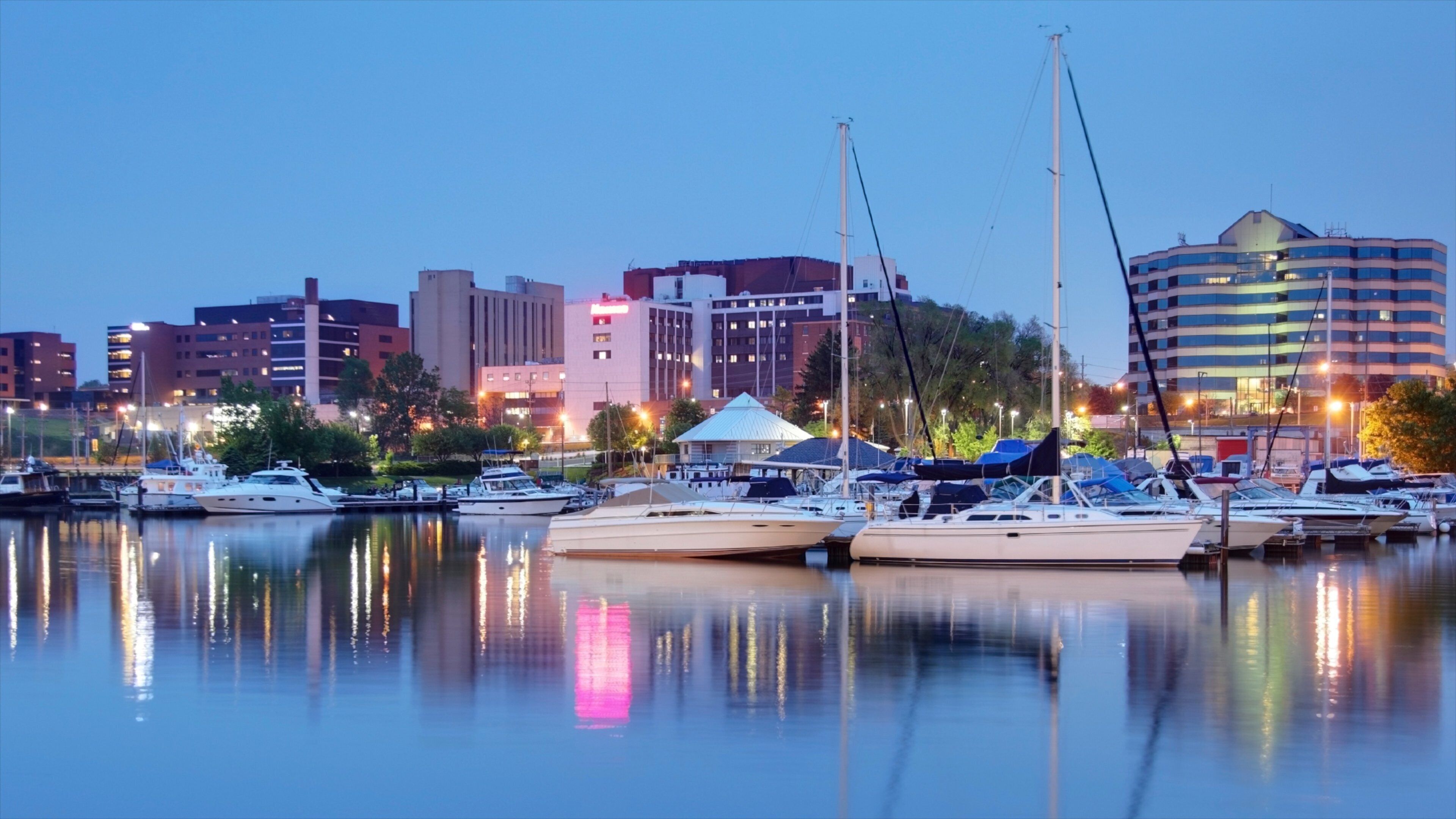 A marina with several yachts docked, a white tent, and a city skyline in the background.
