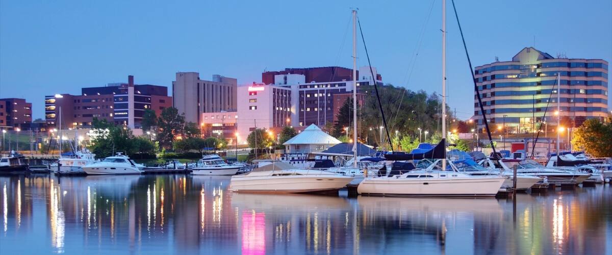 A marina with several yachts docked, a white tent, and a city skyline in the background.