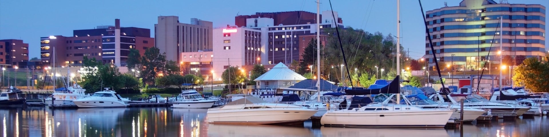 A marina with several yachts docked, a white tent, and a city skyline in the background.