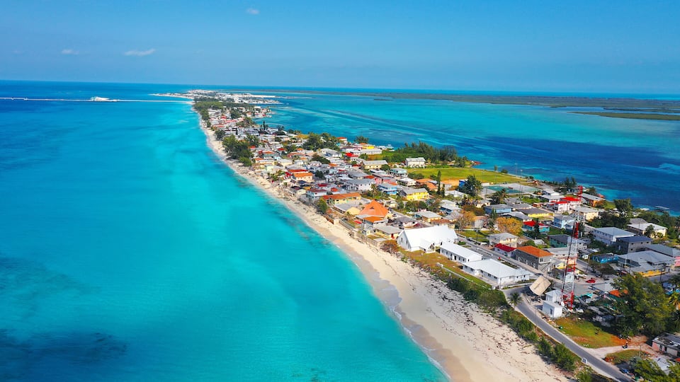 A coastal town with a long beachfront, clear turquoise waters, and a variety of colorful buildings.