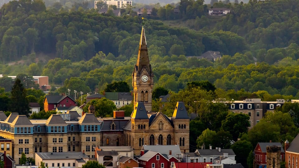 A town with a prominent church featuring a tall steeple and clock tower, surrounded by residential buildings and lush greenery.