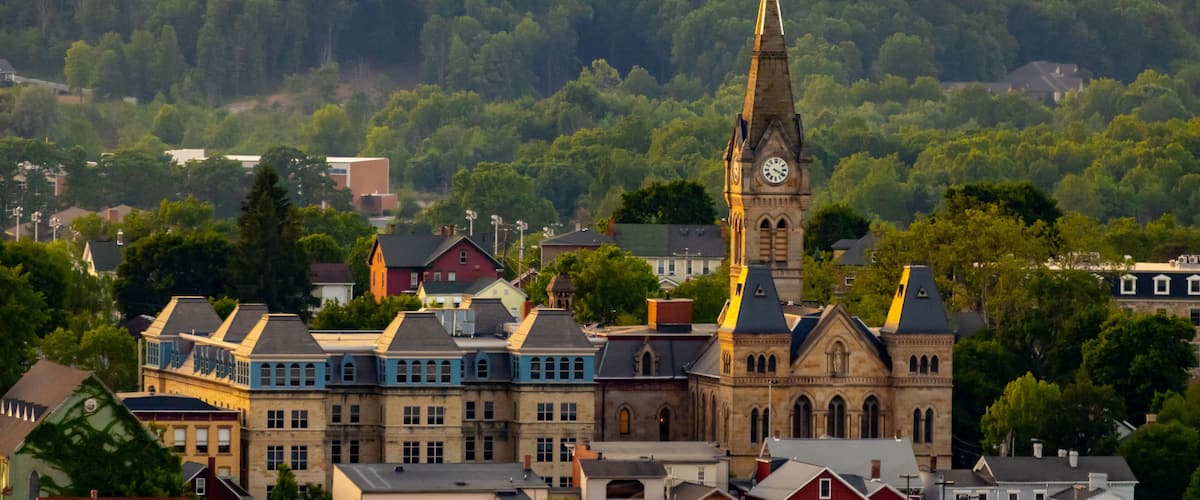 A town with a prominent church featuring a tall steeple and clock tower, surrounded by colorful buildings and dense forested hills in the background.