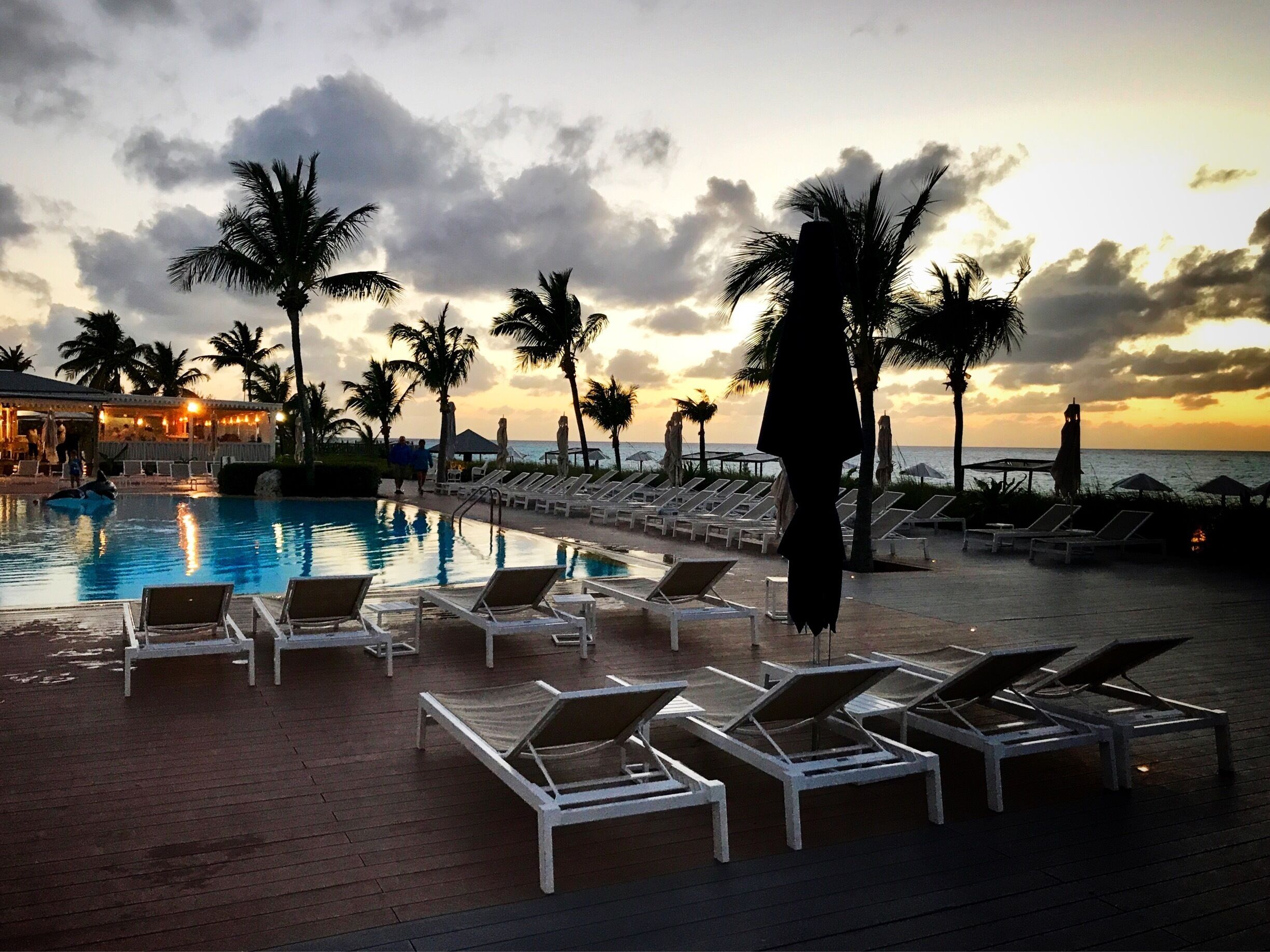 A poolside area with lounge chairs and palm trees at sunset.