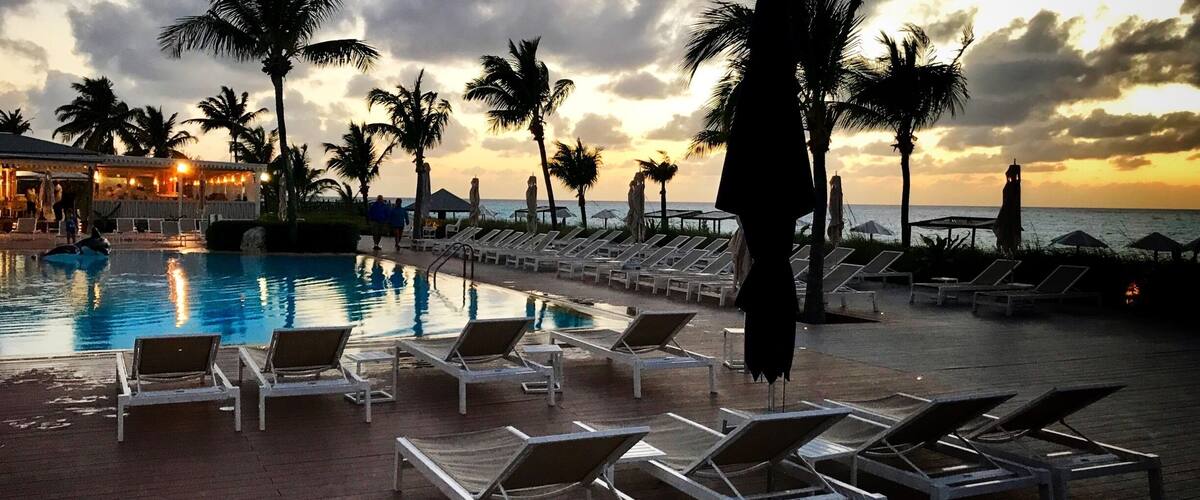 A poolside area with lounge chairs and palm trees at sunset.