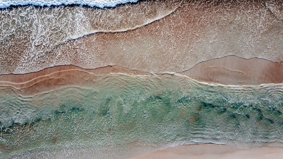 A beach with waves, sand, and a visible underwater layer.