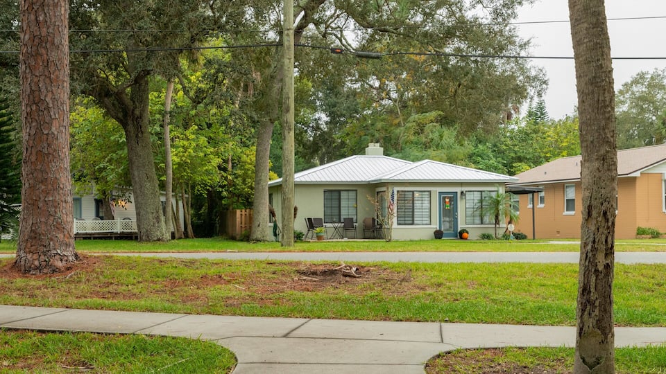 A residential area with a house, trees, and a sidewalk.