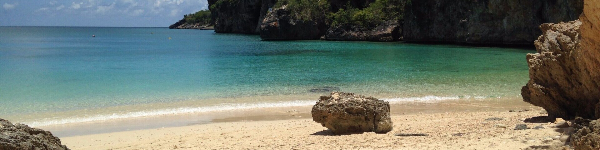 A beach with clear turquoise water, sandy shore, and rocky cliffs.
