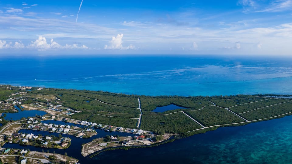 An aerial view of a coastal area with a clear blue sea, a small island with dense greenery, and a settlement with buildings near the shore.
