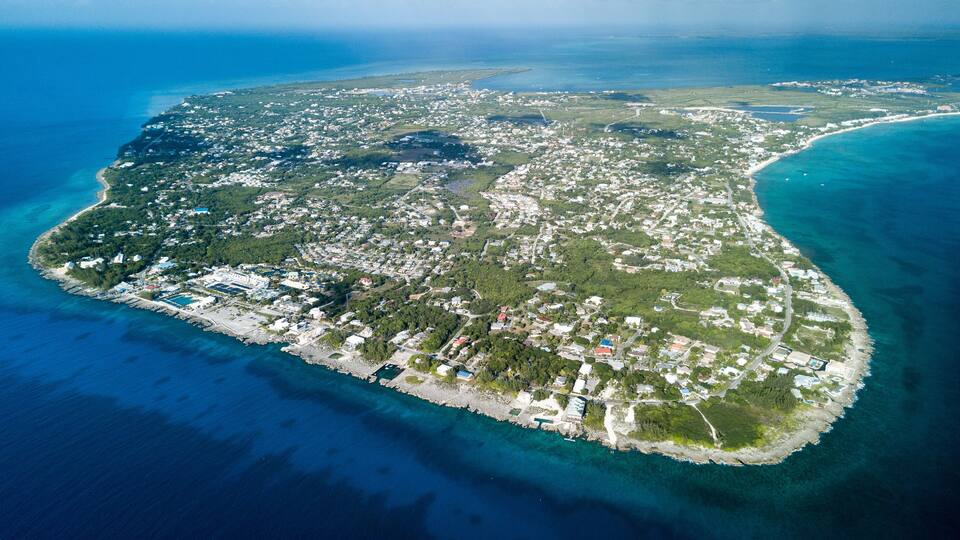 An aerial view of a coastal island with dense residential areas, clear blue waters, and a central lagoon.