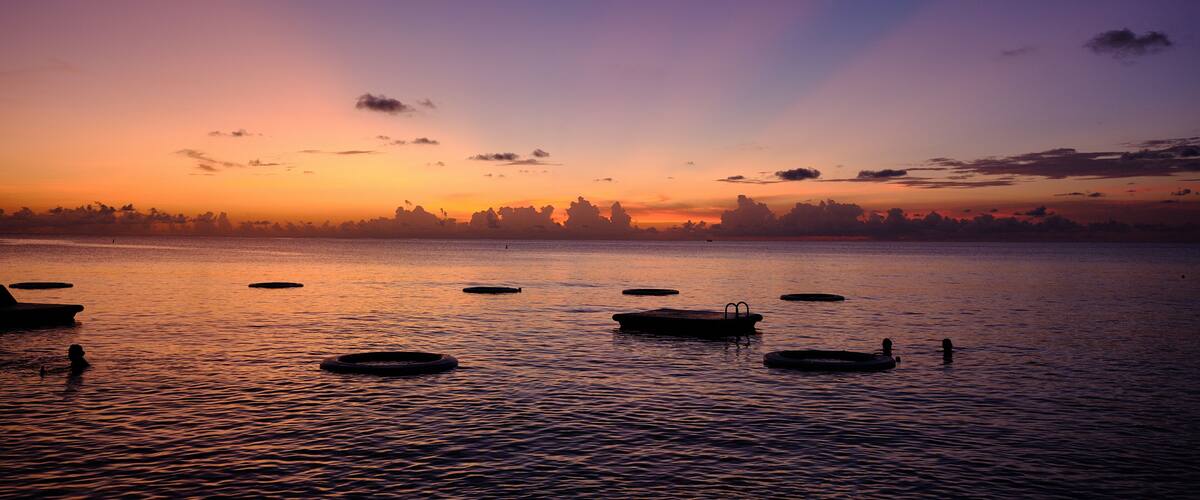 A sunset over a calm lake with several boats and a distant shoreline.