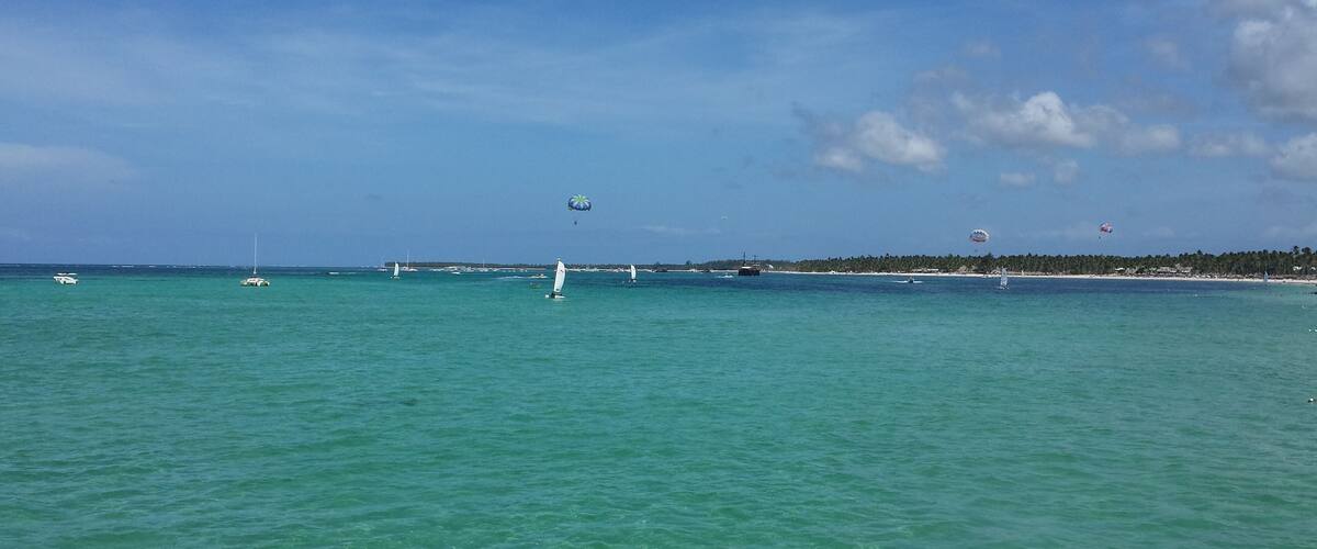 A turquoise sea with sailboats and a distant shoreline with trees.