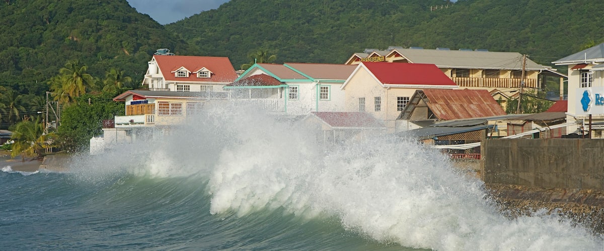 A coastal town with buildings and a large wave crashing onto the shore.