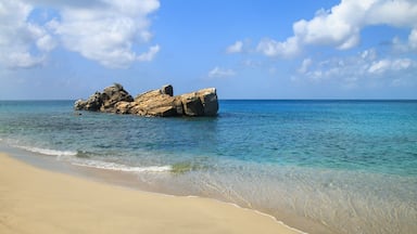 Una playa arenosa con agua turquesa cristalina y un promontorio rocoso en la distancia.