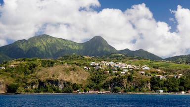 A coastal town with buildings on a hillside, a mountain in the background, and a clear blue sky.