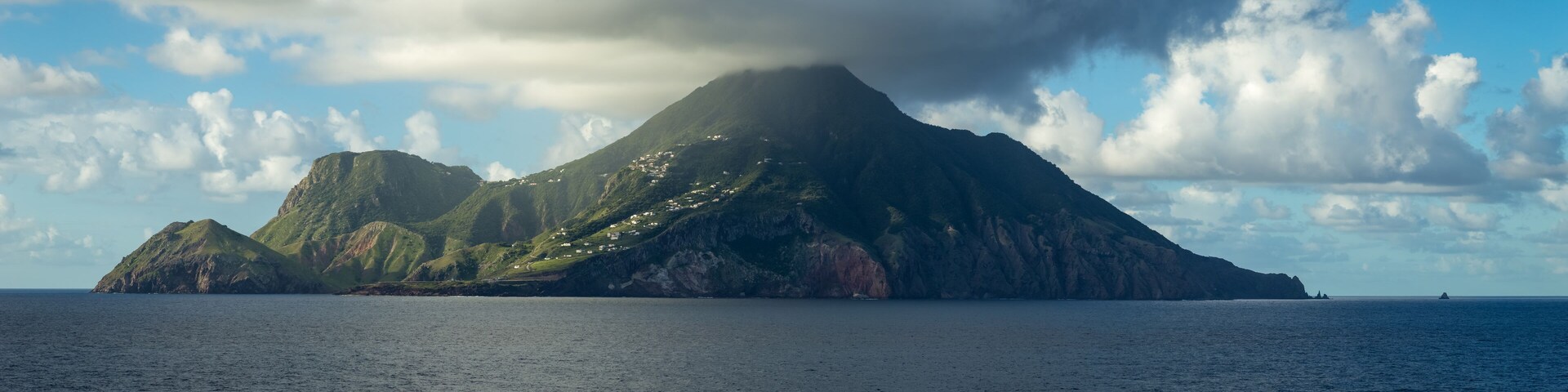 Una isla volcánica con un pico destacado, rodeada por un mar tranquilo y un cielo parcialmente nublado.