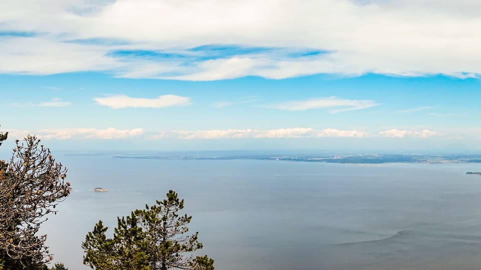 A coastal landscape with a large body of water, several small islands, and a forested hill in the foreground.