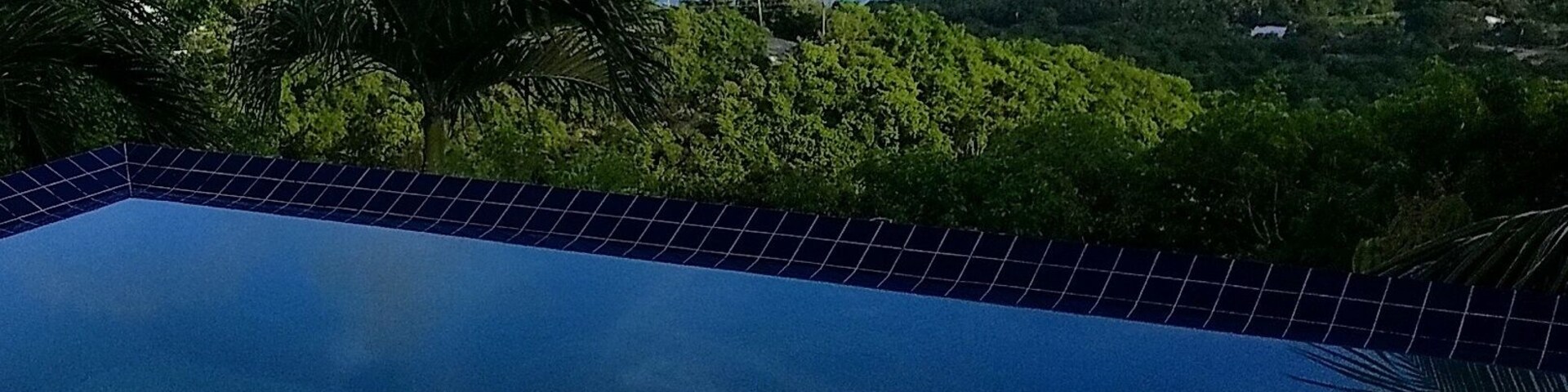 Piscina com vista para uma baía, barcos e paisagem montanhosa.