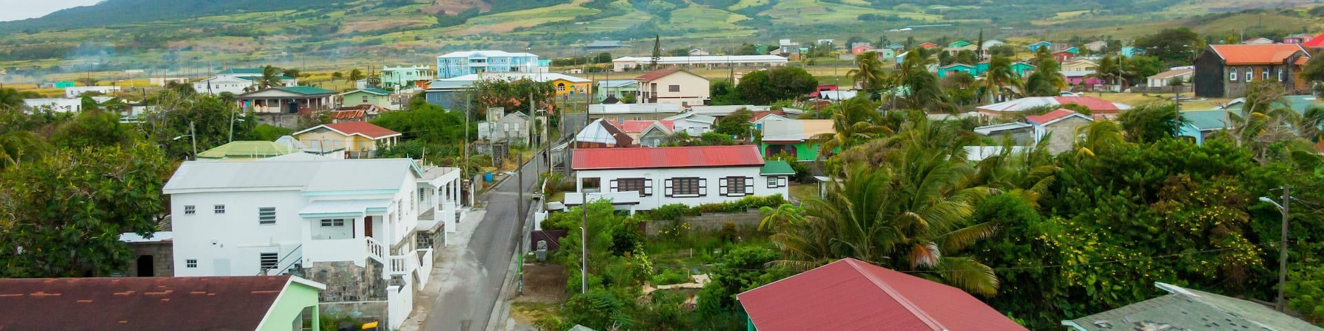 A coastal town with colorful houses, a mountain in the background, and lush greenery.