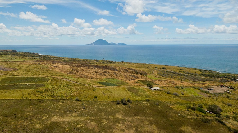 Un paisaje costero con una montaña al fondo, campos verdes y un cielo despejado.