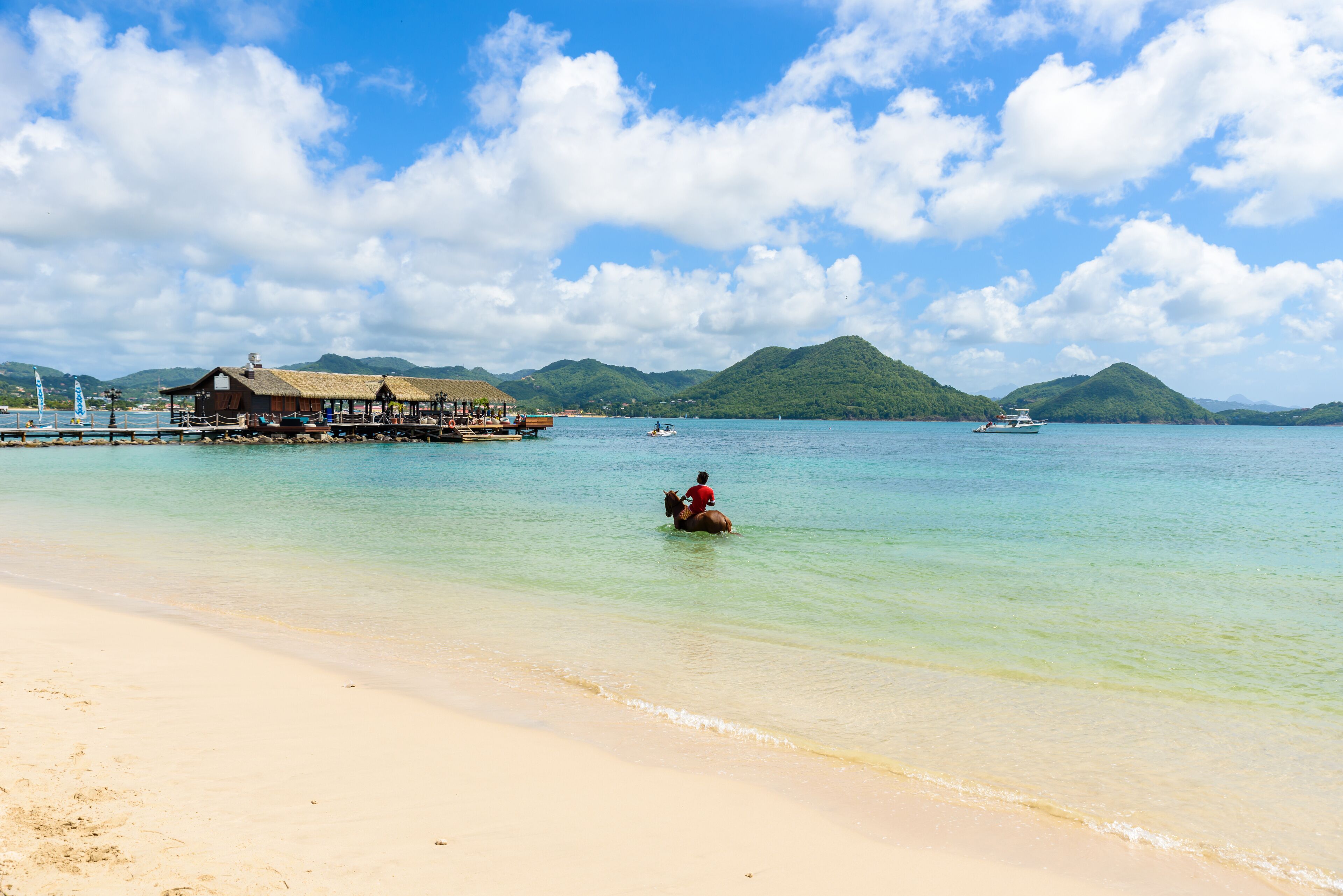 A beach with a wooden pier and a thatched-roof building.