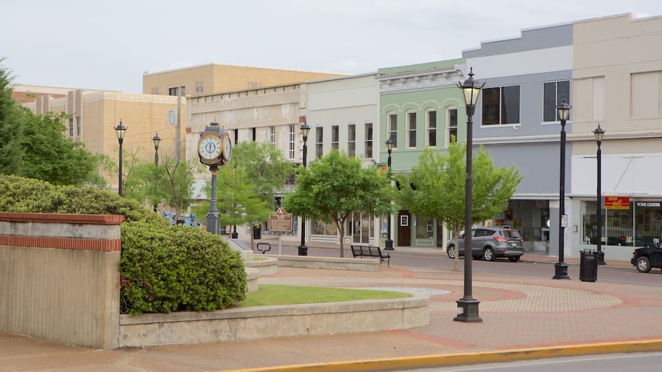 A street with a clock, trees, benches, and buildings.