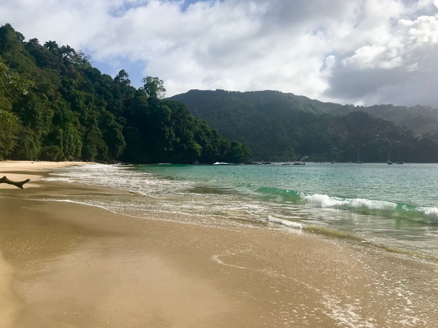 A beach with clear turquoise water, a sandy shore, and a backdrop of lush green hills.