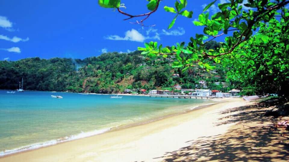 A beach with clear turquoise water, a sandy shore, and a backdrop of lush green hills.