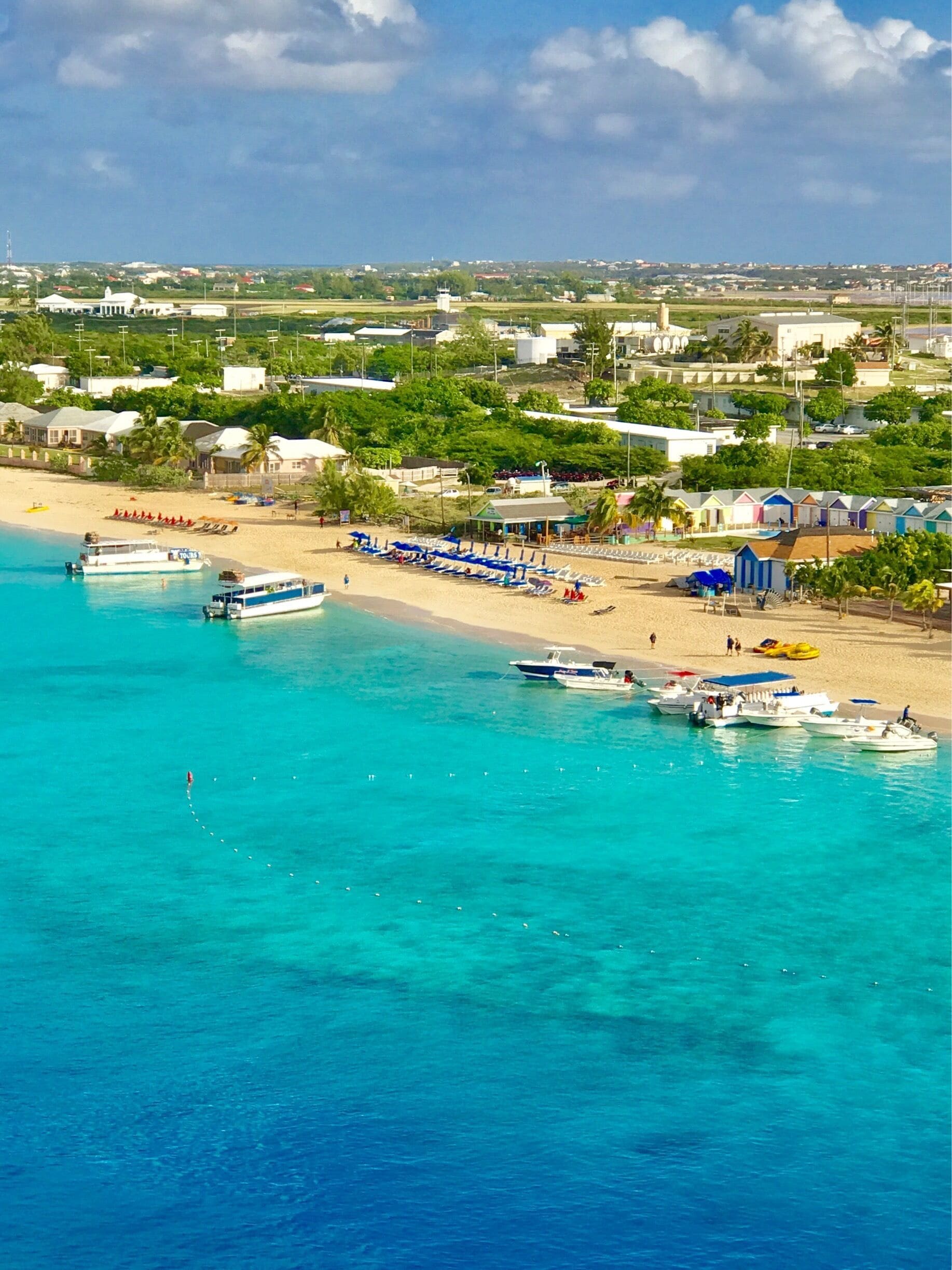 A beach with boats, umbrellas, and a clear blue sea.