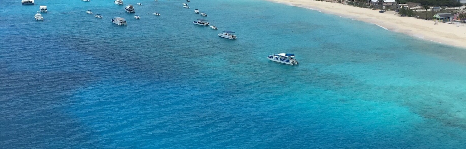 Una zona costera con mar azul cristalino, una playa de arena y varias embarcaciones fondeadas cerca de la costa.