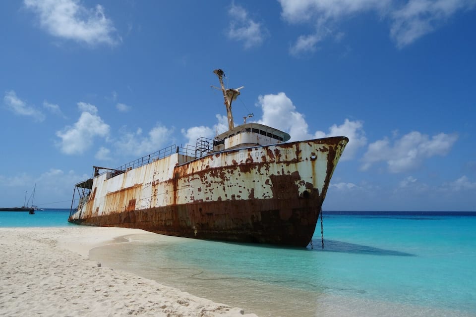 A rusted shipwreck on a sandy beach with clear turquoise water.