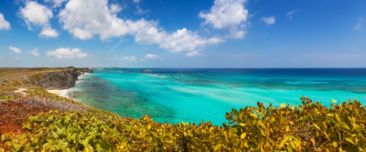 A coastal landscape with turquoise waters, a sandy beach, and green vegetation.