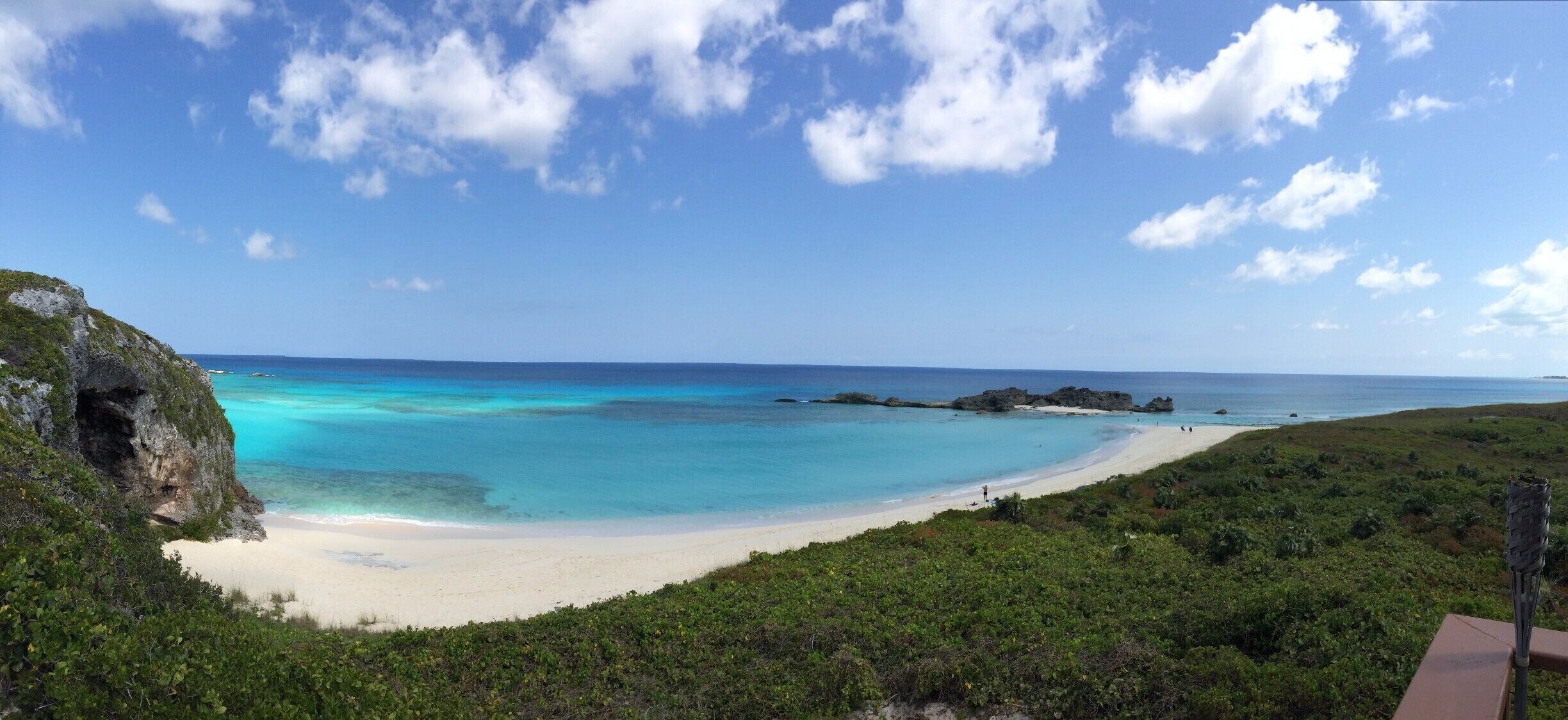 A beach with clear turquoise waters, white sand, and rocky outcrops.