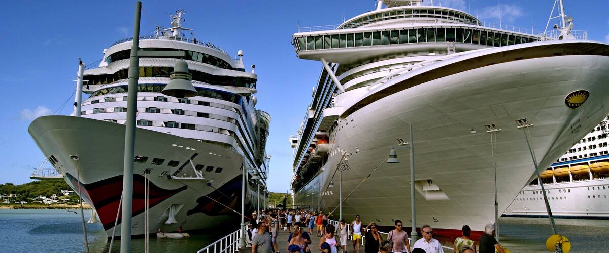 Two large cruise ships docked at a pier with a crowd of people walking along the dock.