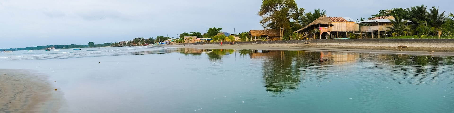 A calm beach with clear water, thatched-roof huts, and palm trees.