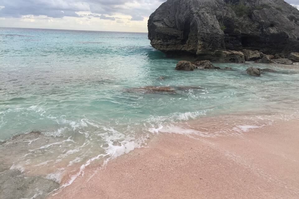 Una playa con agua turquesa cristalina, una gran formación rocosa y un cielo nublado.