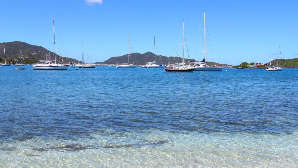 A marina with sailboats docked near a mountainous coastline.
